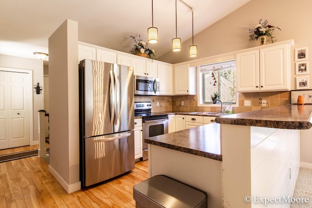 kitchen featuring dark countertops, lofted ceiling, appliances with stainless steel finishes, a peninsula, and a sink