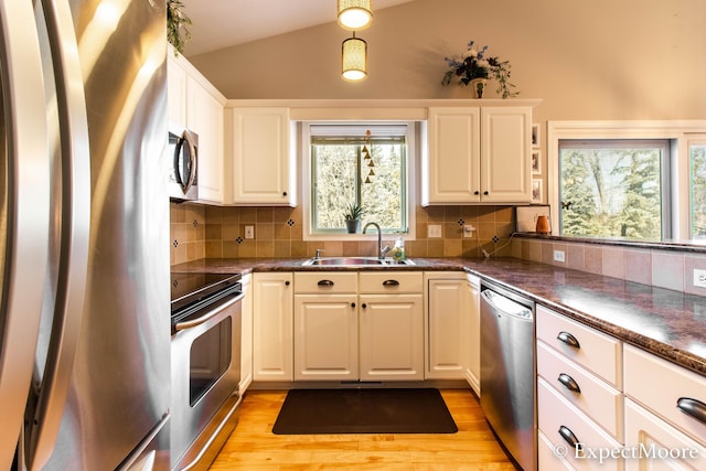 kitchen with lofted ceiling, light wood-style flooring, a sink, stainless steel appliances, and dark countertops