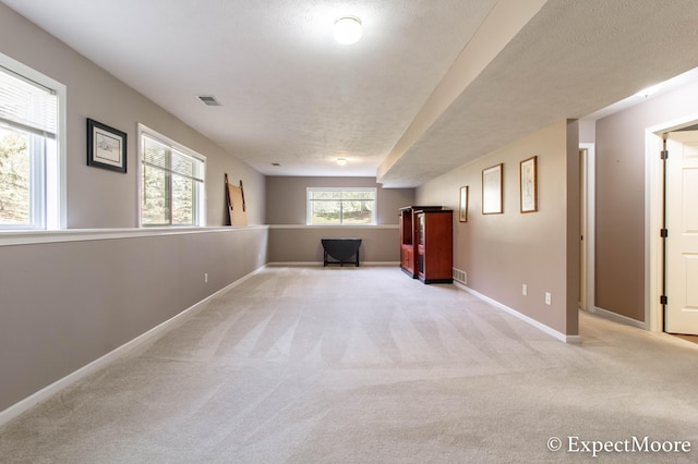 interior space featuring light colored carpet, baseboards, visible vents, and a textured ceiling