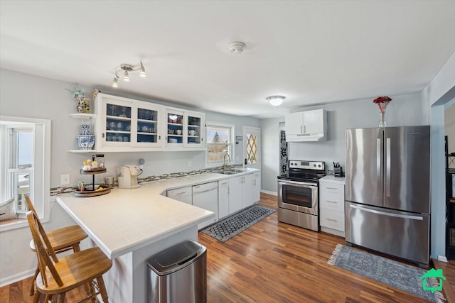 kitchen with a peninsula, dark wood-style flooring, a sink, stainless steel appliances, and a kitchen breakfast bar