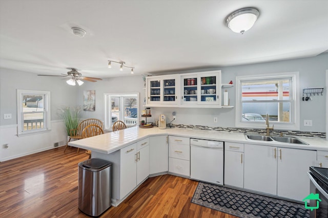 kitchen featuring dark wood-type flooring, light countertops, a peninsula, white dishwasher, and a sink