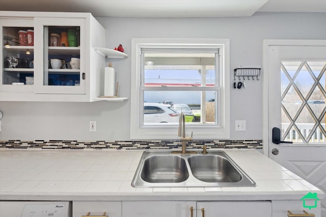 kitchen with backsplash, tile countertops, white cabinetry, and a sink