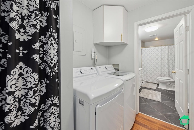 clothes washing area with washer and clothes dryer, visible vents, cabinet space, and wood finished floors