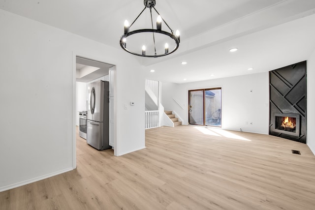 unfurnished living room featuring stairway, visible vents, light wood-style flooring, a notable chandelier, and a large fireplace