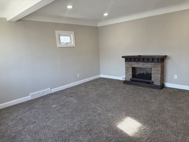 unfurnished living room featuring dark colored carpet, visible vents, baseboards, and a stone fireplace