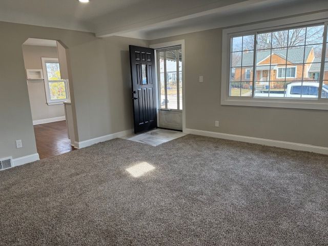 carpeted entrance foyer featuring beamed ceiling, plenty of natural light, baseboards, and arched walkways