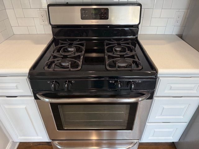 room details with stainless steel gas range oven, backsplash, white cabinetry, and light countertops