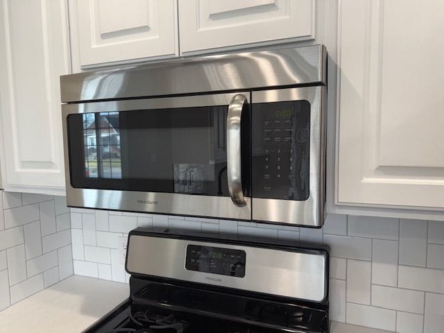 interior details with tasteful backsplash, appliances with stainless steel finishes, white cabinets, and light countertops