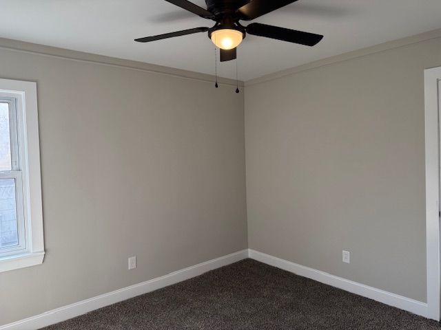 unfurnished room with dark colored carpet, baseboards, ornamental molding, and a ceiling fan