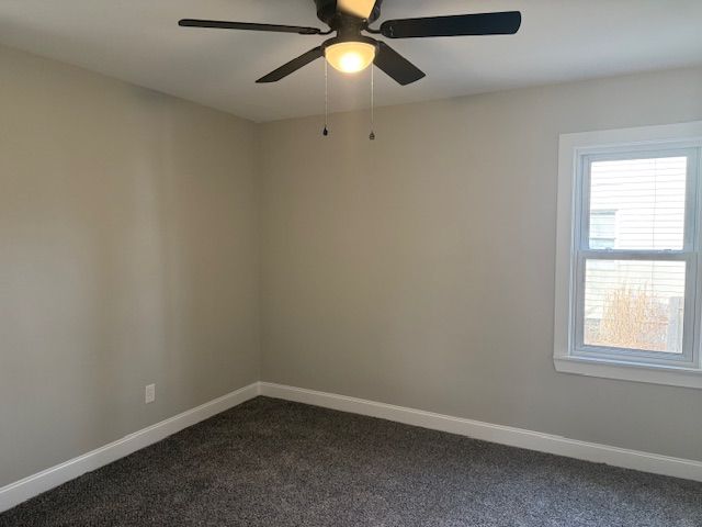 spare room with ceiling fan, baseboards, and dark colored carpet