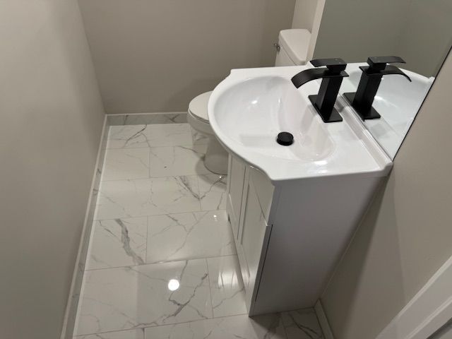 bathroom with marble finish floor, toilet, vanity, and baseboards