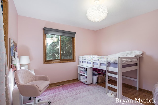 bedroom with a notable chandelier, wood finished floors, visible vents, and baseboards