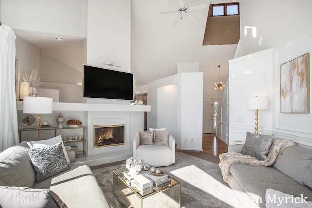 living area featuring a glass covered fireplace, a high ceiling, a ceiling fan, and wood finished floors