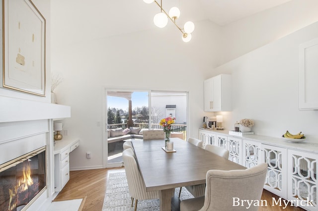 dining space with baseboards, high vaulted ceiling, an inviting chandelier, light wood-style floors, and a glass covered fireplace