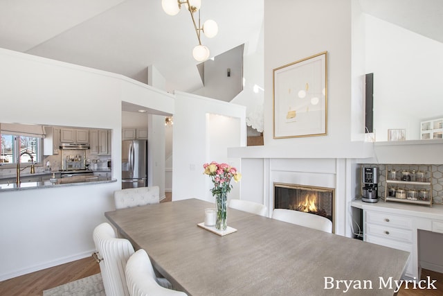 dining area with a glass covered fireplace, wood finished floors, and high vaulted ceiling