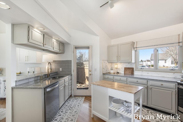 kitchen featuring lofted ceiling, a sink, stainless steel appliances, wood counters, and backsplash