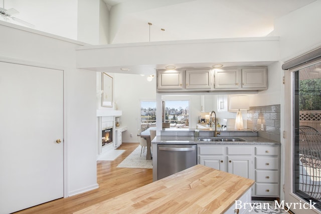 kitchen with a fireplace with flush hearth, a sink, light wood finished floors, decorative backsplash, and dishwasher