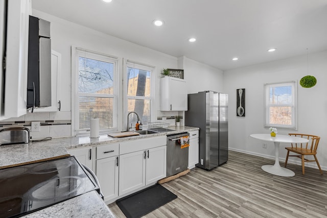 kitchen with a sink, tasteful backsplash, appliances with stainless steel finishes, white cabinets, and light wood finished floors