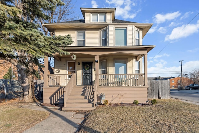 american foursquare style home featuring a porch and fence