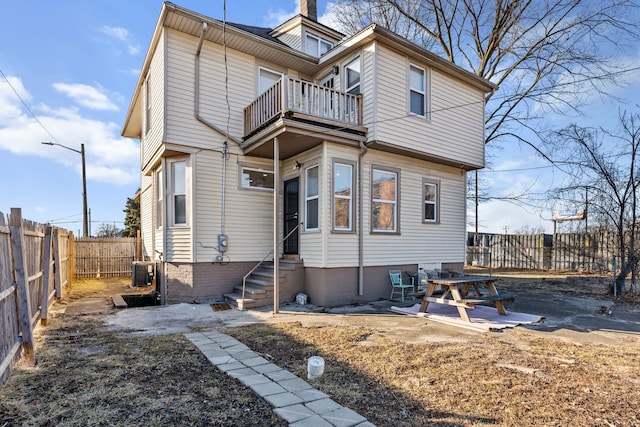 view of front of house with entry steps, central AC, a fenced backyard, a balcony, and a chimney