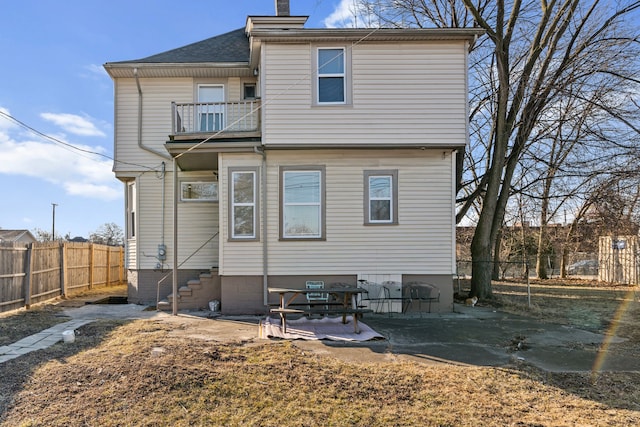 back of property with entry steps, fence, a balcony, a chimney, and a patio area