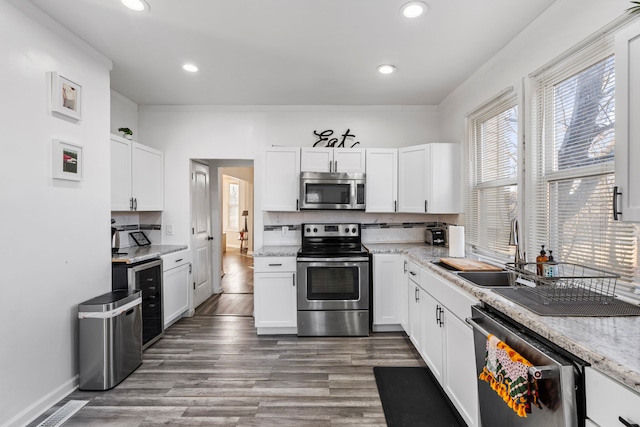 kitchen with a sink, stainless steel appliances, backsplash, and white cabinetry