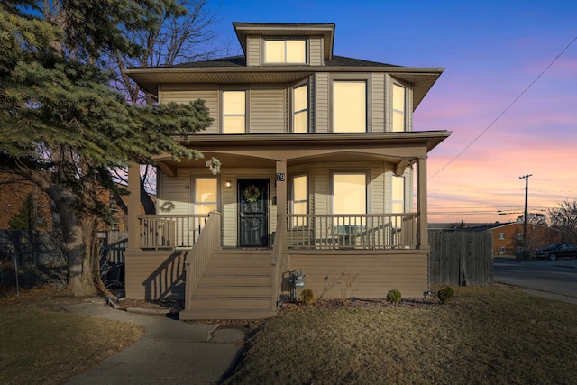 american foursquare style home featuring a porch and fence