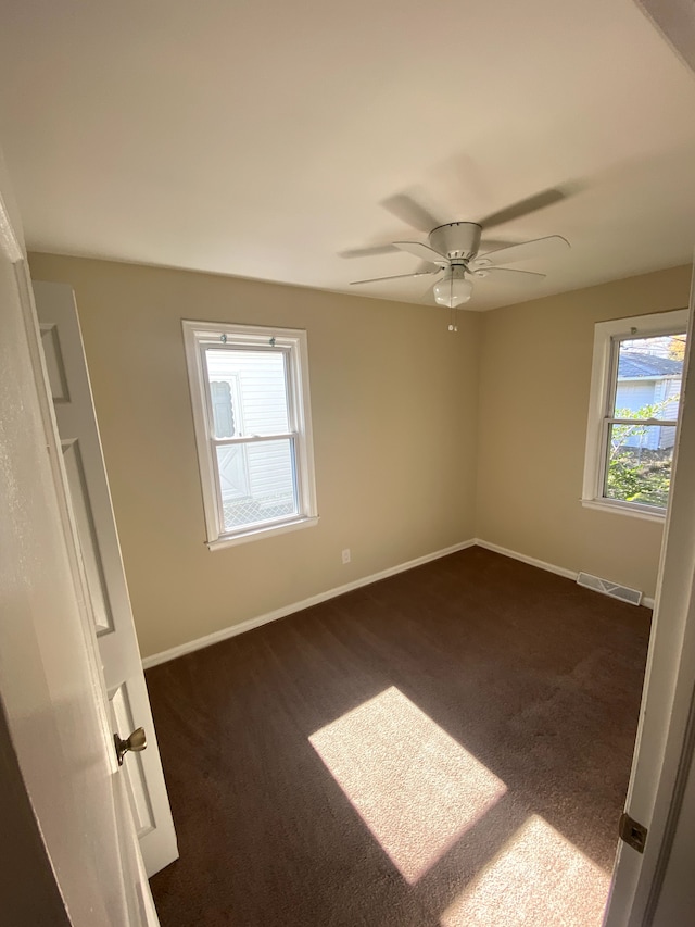 unfurnished room with visible vents, baseboards, dark carpet, and ceiling fan