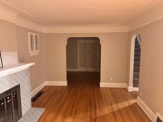 unfurnished living room with visible vents, baseboards, arched walkways, a tile fireplace, and wood-type flooring