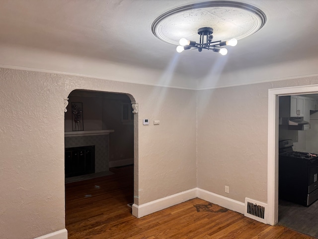 unfurnished dining area featuring visible vents, wood finished floors, arched walkways, a fireplace, and a chandelier