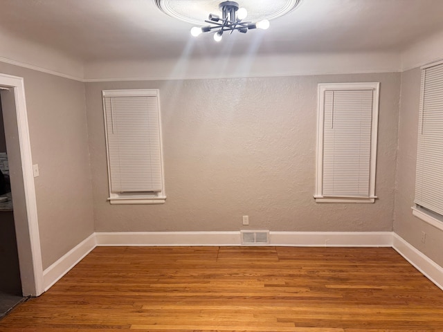 unfurnished room with visible vents, wood finished floors, an inviting chandelier, baseboards, and a textured wall