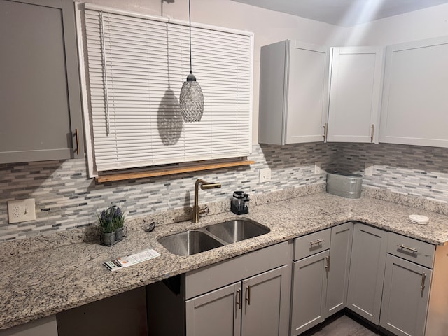 kitchen featuring gray cabinetry, light stone countertops, backsplash, and a sink