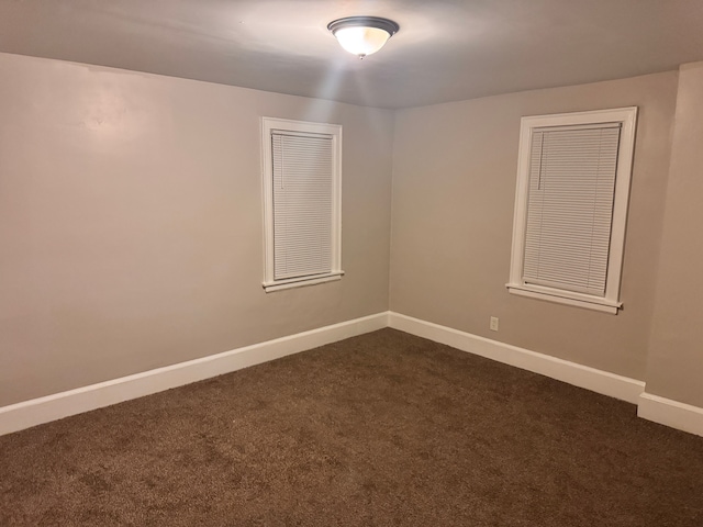 unfurnished room featuring baseboards and dark carpet