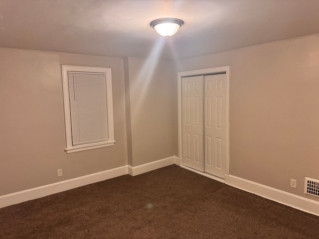 unfurnished bedroom with dark colored carpet, a closet, baseboards, and visible vents