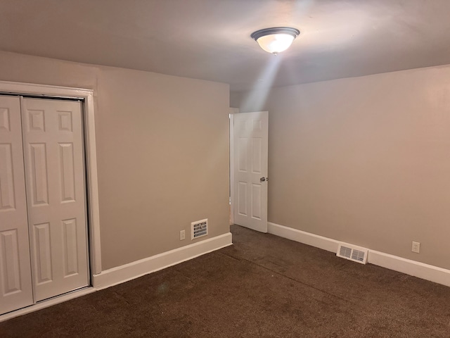 unfurnished bedroom featuring dark colored carpet, visible vents, baseboards, and a closet