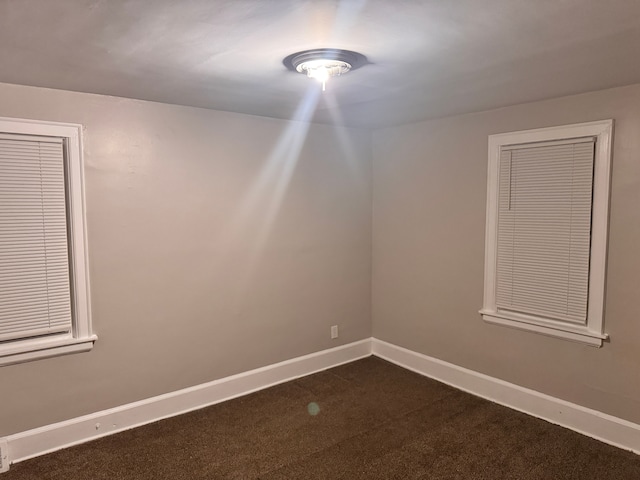 unfurnished room with dark colored carpet and baseboards