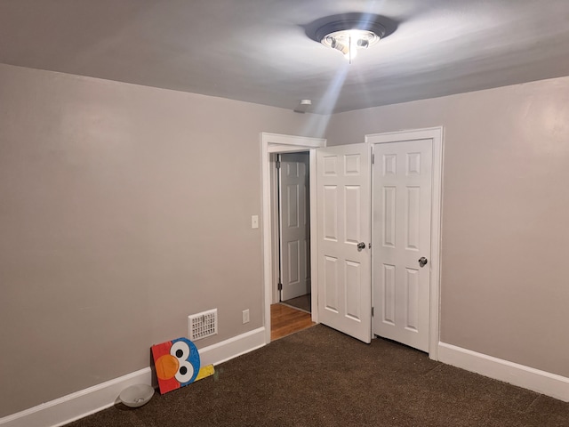 unfurnished bedroom featuring visible vents, baseboards, and dark carpet