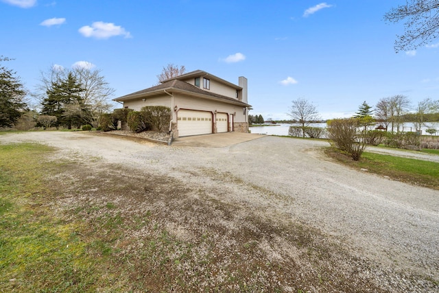 view of property exterior featuring driveway, a chimney, and a water view