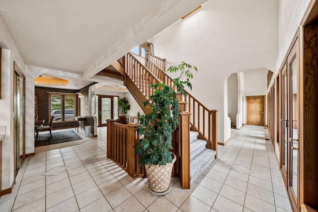 foyer with arched walkways, light tile patterned floors, a textured ceiling, and stairs