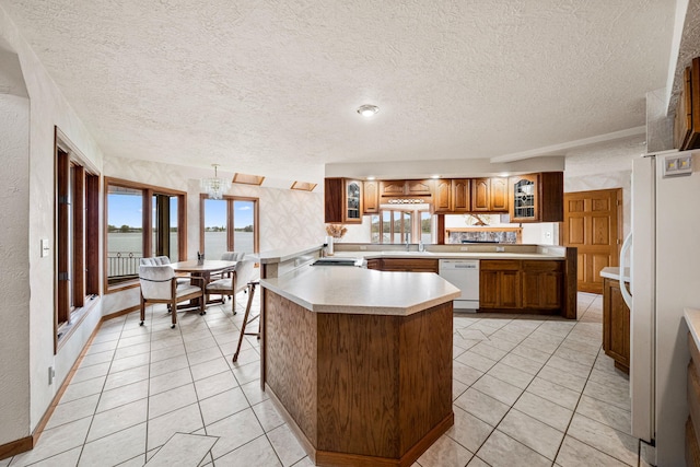 kitchen with glass insert cabinets, white appliances, brown cabinets, and light countertops