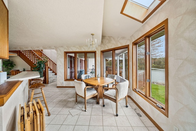 dining space featuring baseboards, a water view, lofted ceiling with skylight, stairs, and an inviting chandelier