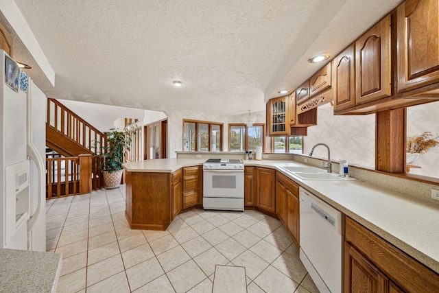 kitchen with white appliances, brown cabinetry, a peninsula, and a sink