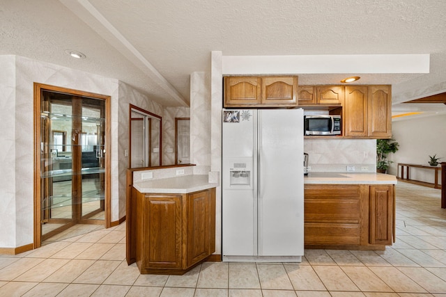 kitchen featuring stainless steel microwave, brown cabinets, white refrigerator with ice dispenser, and light countertops