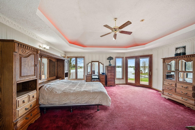 bedroom with carpet floors, a textured ceiling, a raised ceiling, a ceiling fan, and access to outside