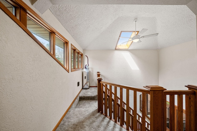 hallway featuring lofted ceiling with skylight, an upstairs landing, carpet, and a textured wall