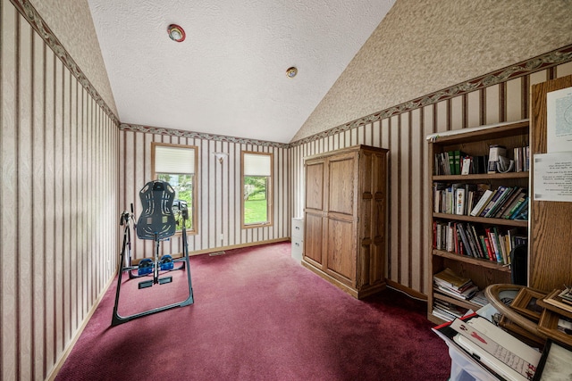 exercise area with wallpapered walls, baseboards, dark carpet, vaulted ceiling, and a textured ceiling