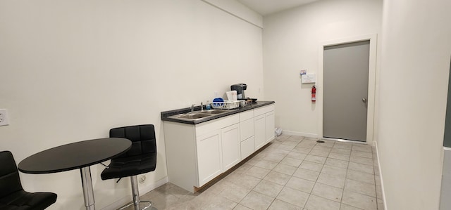 kitchen with baseboards, light tile patterned flooring, a sink, white cabinetry, and dark countertops