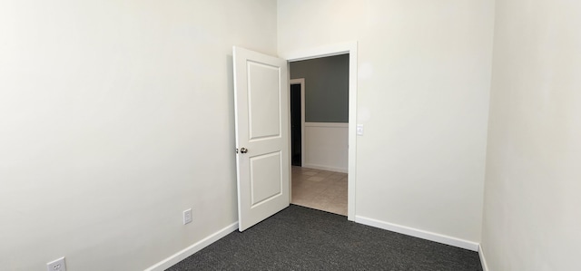 unfurnished room featuring baseboards and dark carpet