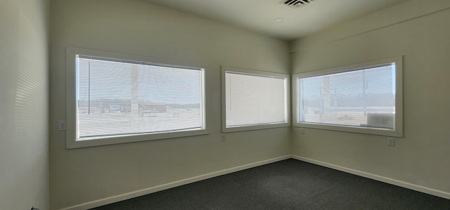 unfurnished room with baseboards, plenty of natural light, visible vents, and dark carpet