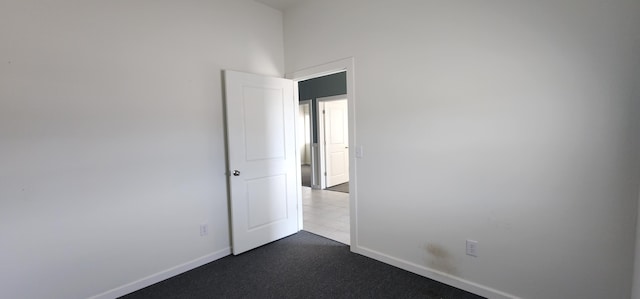 spare room with baseboards and dark colored carpet